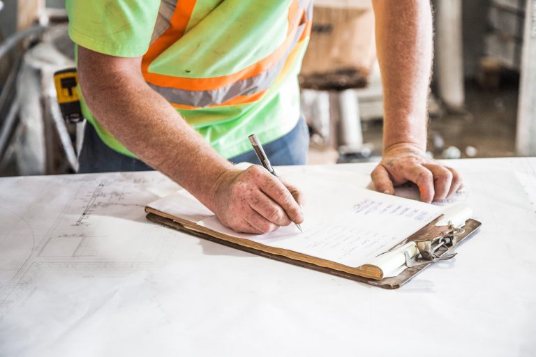 Construction worker in a high vis with hard hat writing on a clipboard